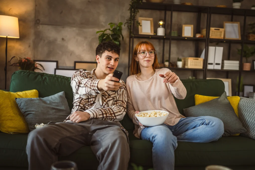 shutterstock_2442553569 - VIPshow Dva lidé, muž a žena, sledují televizi, mají k tomu popcorn