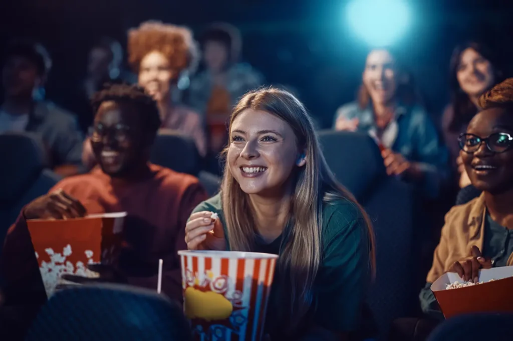 shutterstock_2570161265 - VIPshow Žena s popcornem kouká na filmové plátno a usmívá se.