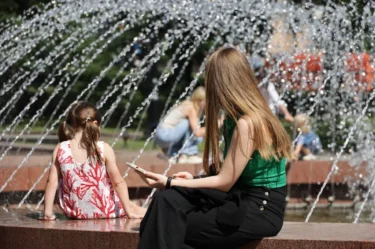 Žena a další lidé se ochlazují u fontány za slunečného dne