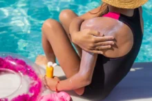 Žena v černých plavkách se natírá krémem, který drží v druhé ruce