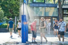 Lidé se ochlazují pod veřejným rozprašovačem vody v rozpáleném městě