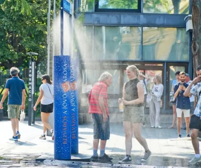Lidé se ochlazují pod veřejným rozprašovačem vody v rozpáleném městě