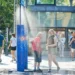 Lidé se ochlazují pod veřejným rozprašovačem vody v rozpáleném městě