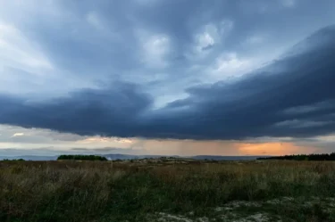 Bouřkové mraky, přes které prosvítá slunce, se kumulují nad krajinou