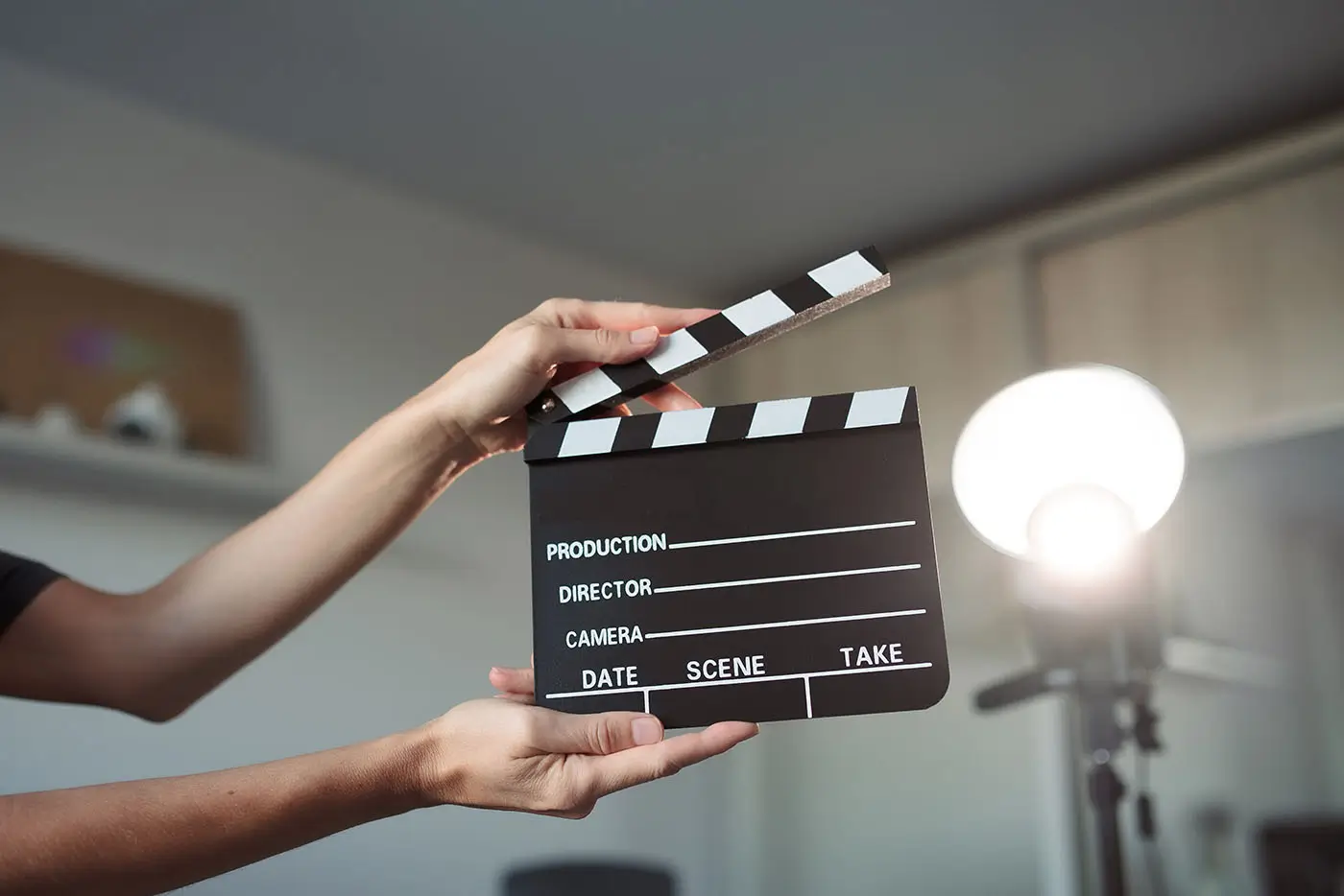 shutterstock_2728887833 - VIPshow Ruce drží filmovou klapku a v pozadí svítí lampa