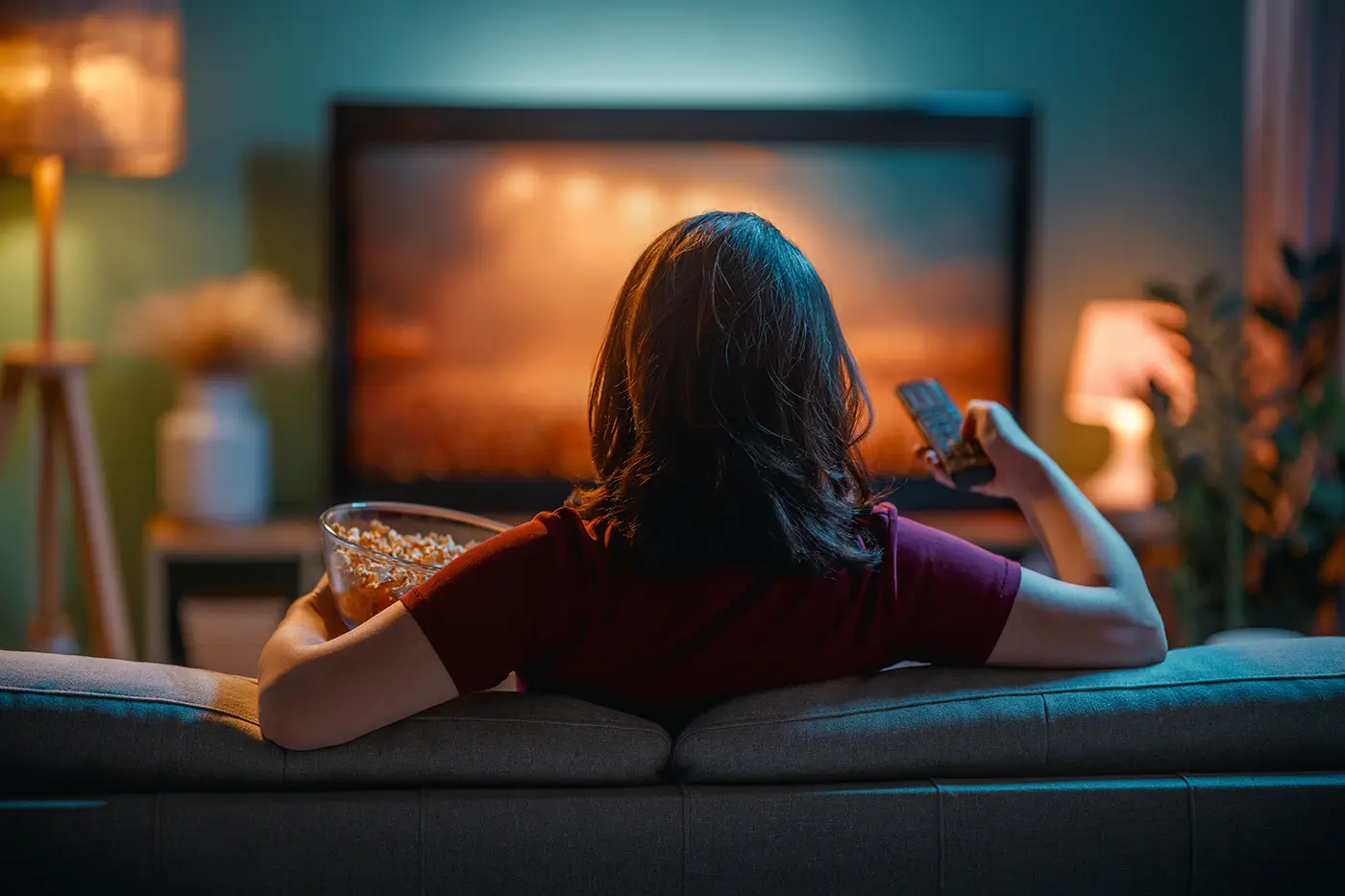 Žena sedí na gauči a dívá se na televizi.