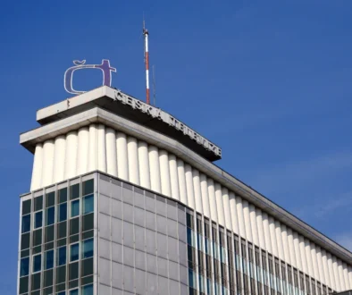 Logo společnosti České televize na rohu vysoké budovy, nad ní jsou modrá oblaka