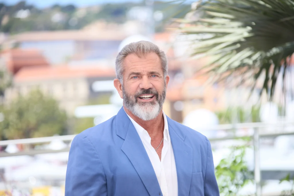 shutterstock_426626110 - VIPshow Muž v bilé rozhalence světle modrém saku, v pozadí je přímořské letovisko