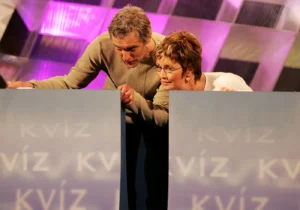 Muž a žena se k sobě naklání a na něco se dívají ve studiu