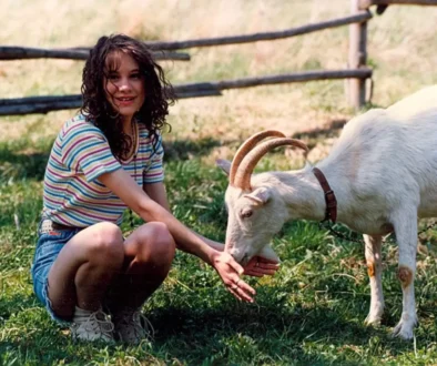 Žena klečí u kozy a krmí ji trávou