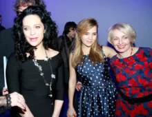 Tři ženy v letních slavnostních šatech na party, za nimi je modré pozadí a další lidé