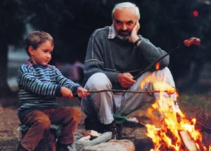 Starší muž sedí s dítětem u ohně a povídají si