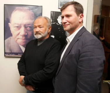 Dva muži v oblecích stojí u fotografie dalšího muže, synové a otec