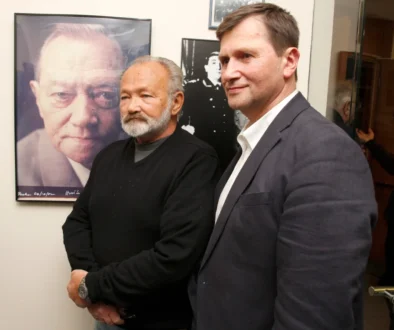 Dva muži v oblecích stojí u fotografie dalšího muže, synové a otec