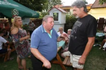 Dva muži si spolupovídají na zahradě u slunečníku, jeden je obézní, druhý vysoký