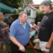 Dva muži si spolupovídají na zahradě u slunečníku, jeden je obézní, druhý vysoký
