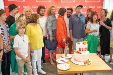 Lidé stojí před plakátem cihlové barvy a fotí se s dortem