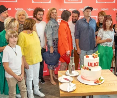 Lidé stojí před plakátem cihlové barvy a fotí se s dortem