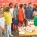 Lidé stojí před plakátem cihlové barvy a fotí se s dortem