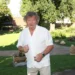 Starší muž v bílé košili a světlých kalhotách stojí na trávě