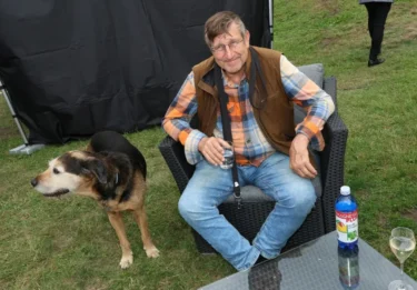 Muž sedí v křesle na trávníku a vedle něj stojí pes