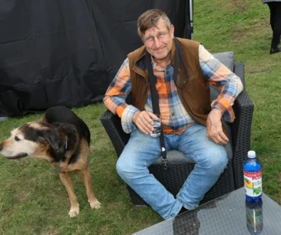 Muž sedí v křesle na trávníku a vedle něj stojí pes