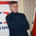 Muž v černém obleku stojí před plakátem s logem České televize