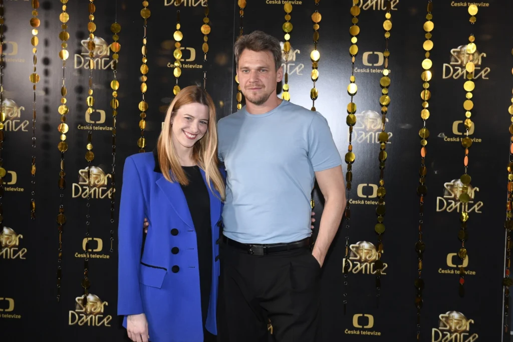 profimedia-1093273282 - VIPshow Usmívající se dvojice, oba jsou v modrém oblečení, žena má sako, muž tričko, za nimi je pozadí s nápisy StarDance