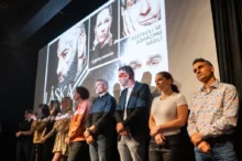 Skupina lidí na pódiu, za nimi je plakát a na něm fotografie a název Láska nebolí