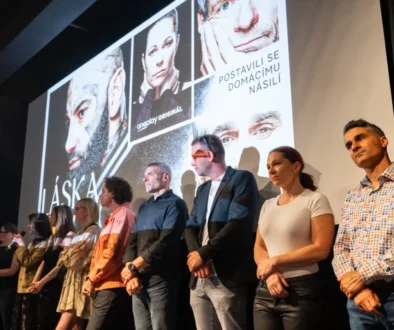 Skupina lidí na pódiu, za nimi je plakát a na něm fotografie a název Láska nebolí