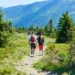 Dva turisté jsou pěšinou kolem se tyčí vysoké hory plné lesů