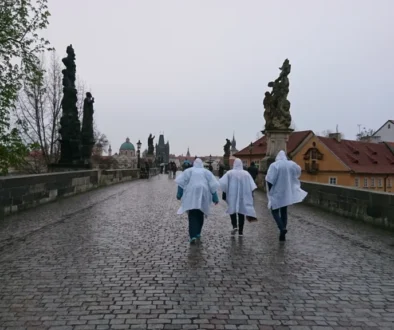 tři lidé v modrých pláštěnkách běží po kamenném mostě