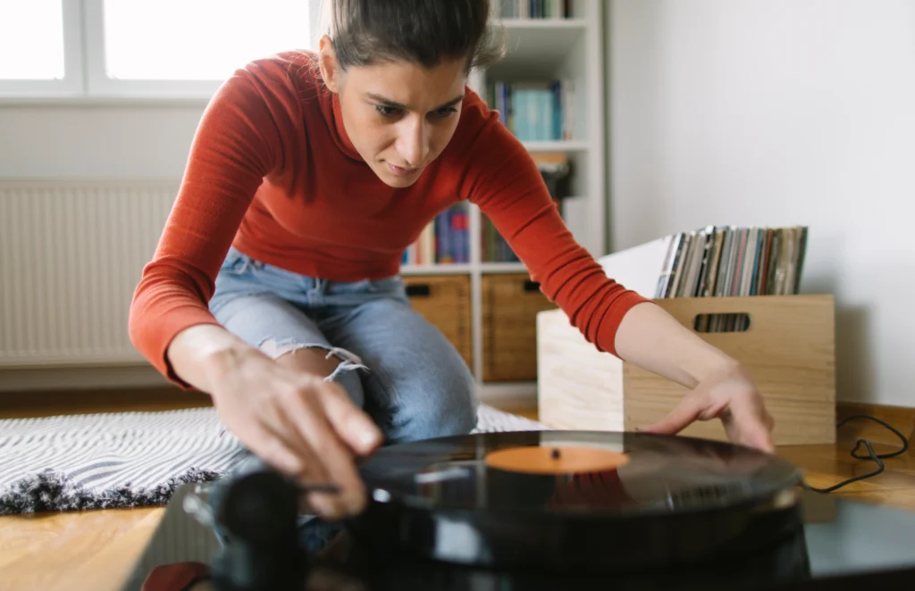 shutterstock_1676311618 - VIPshow Žena v červeném tričku a džínech si pouští vinylovou desku na gramofononu