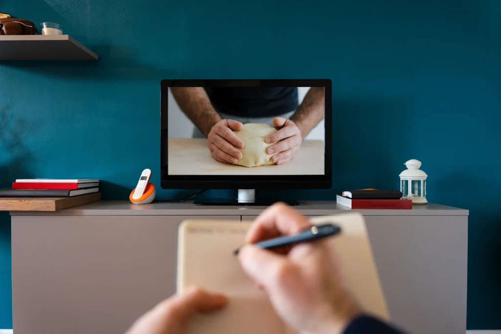 shutterstock_1897063534 - VIPshow Muž drží v ruce pero a podle pořadu v televizi, kde muž válí těsto, si zapisuje recept