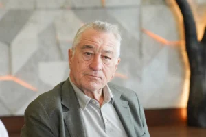 Starší muž s šedivými vlasy a v šedém saku naklání hlavu na stranu