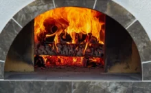 Rozpálená kamenná pec na pizzu s hořícími poleny uvnitř
