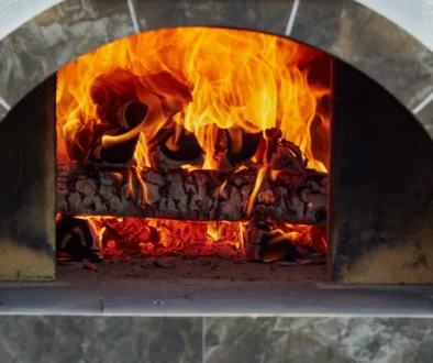 Rozpálená kamenná pec na pizzu s hořícími poleny uvnitř