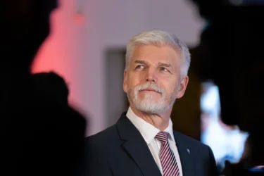 Starší muž s šedými vlasy a bradkou v obleku s červenou kravatou hledí vzhůru