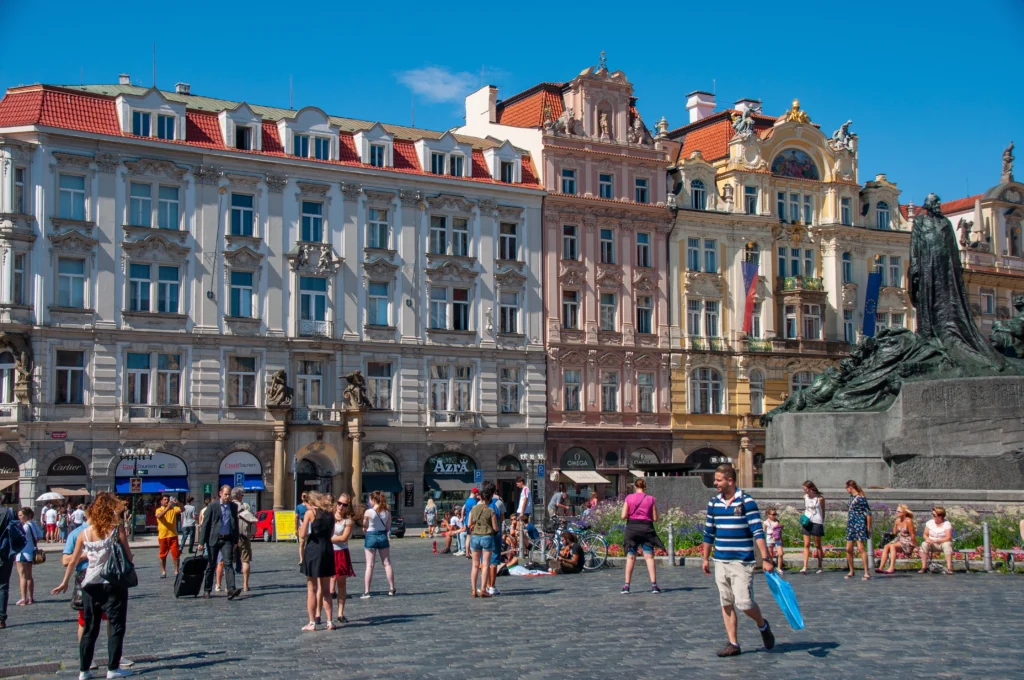 Domy na náměstí, rozpálená ulice, úplně modré nebe a turisté v letním oblečení