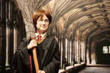 Vosková figurína připomínající známého Harryho Pottera, má kouzelnický hábit, koště a kulaté brýle