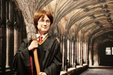 Vosková figurína připomínající známého Harryho Pottera, má kouzelnický hábit, koště a kulaté brýle