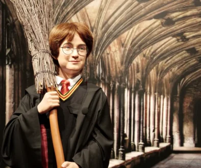 Vosková figurína připomínající známého Harryho Pottera, má kouzelnický hábit, koště a kulaté brýle