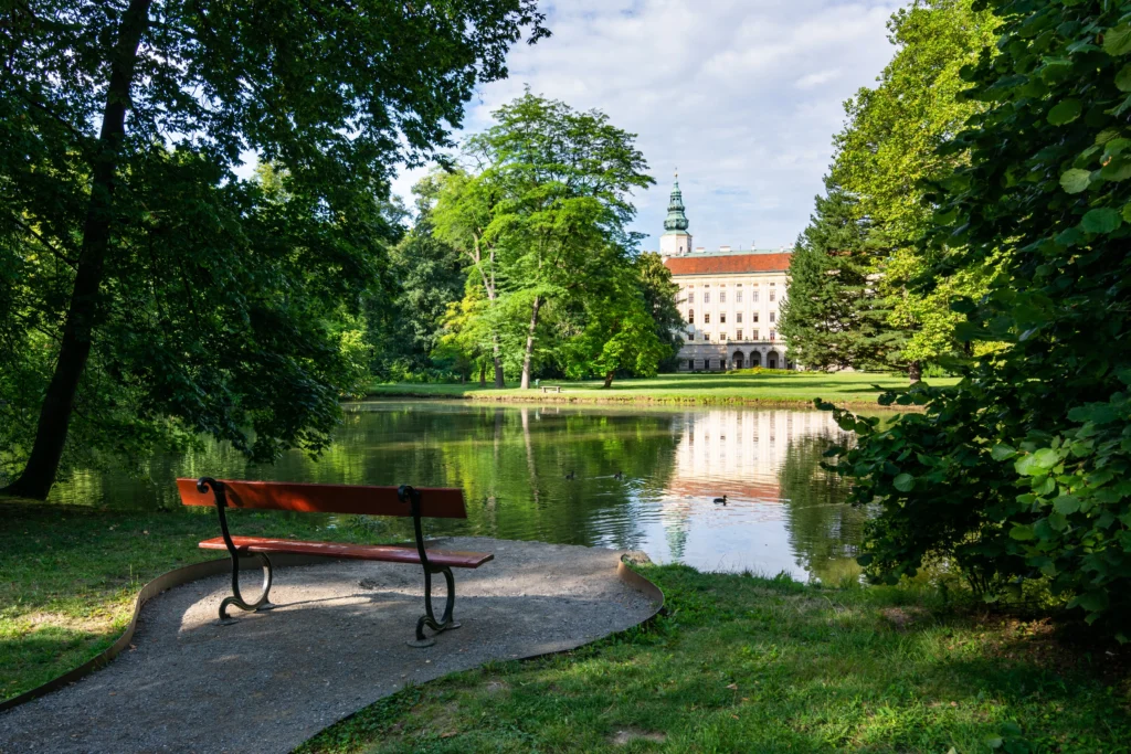 shutterstock_2437510323 - VIPshow Arcibiskupský zámek v Kroměříži, pohled z lavičky přes jezero a zelené stromy