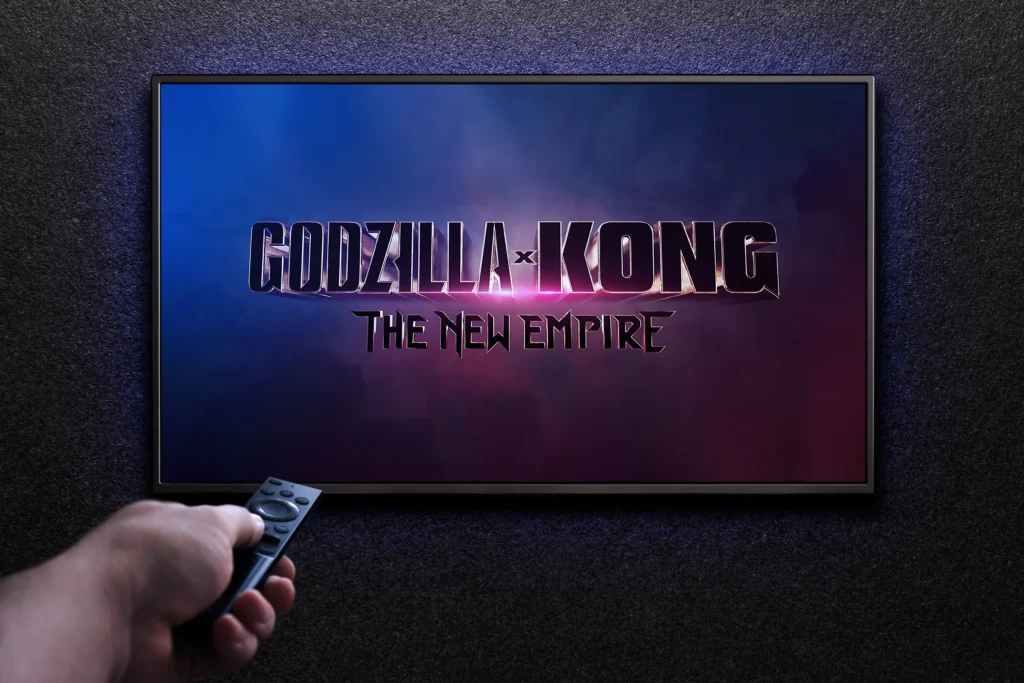 Ruka s ovladačem míří na televizní obrazovku, na ní je nápis Godzila x Kong