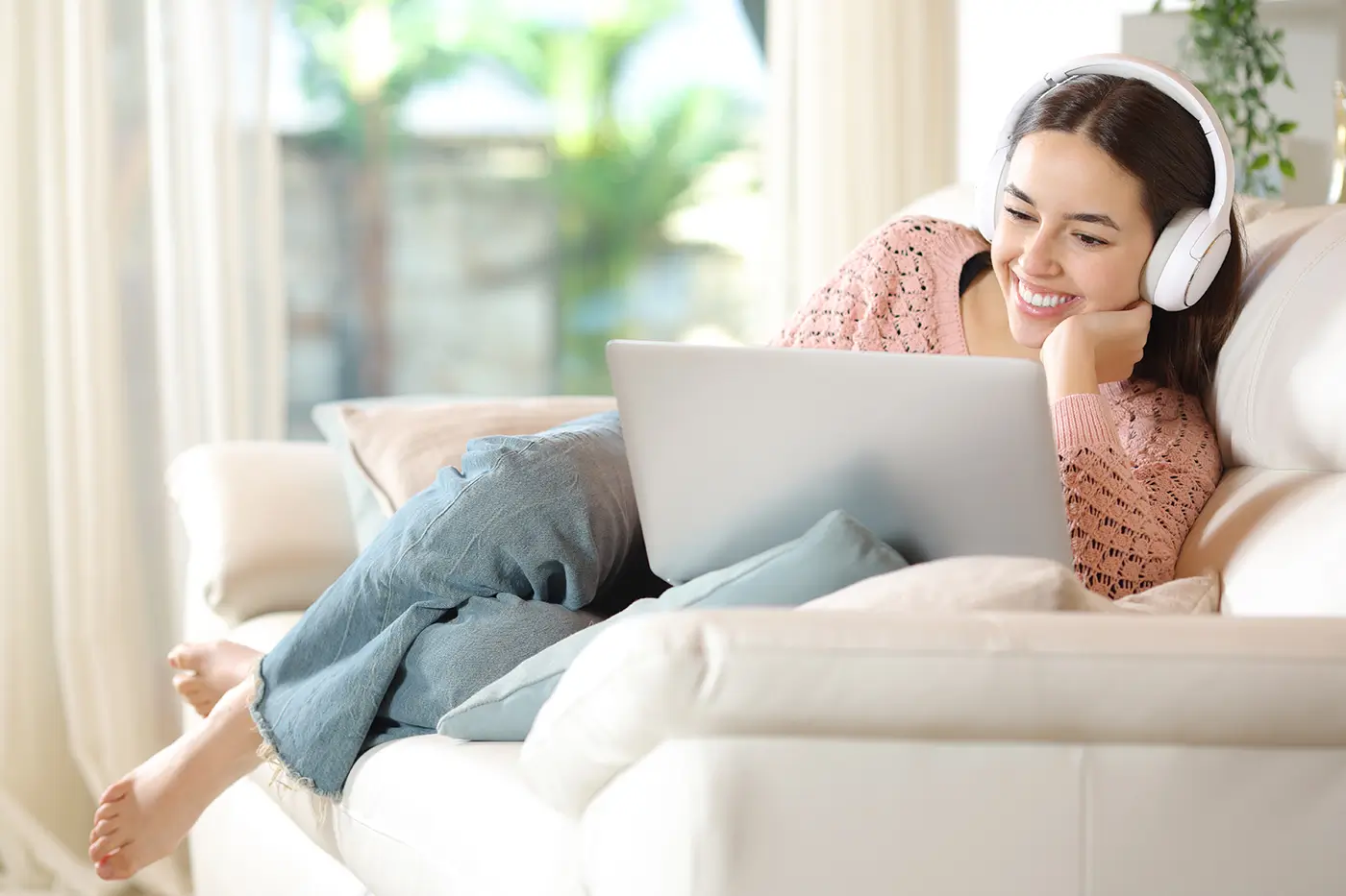 shutterstock_2467076541 - VIPshow Žena se sluchátky na uších leží na pohovce a dívá se na počítač