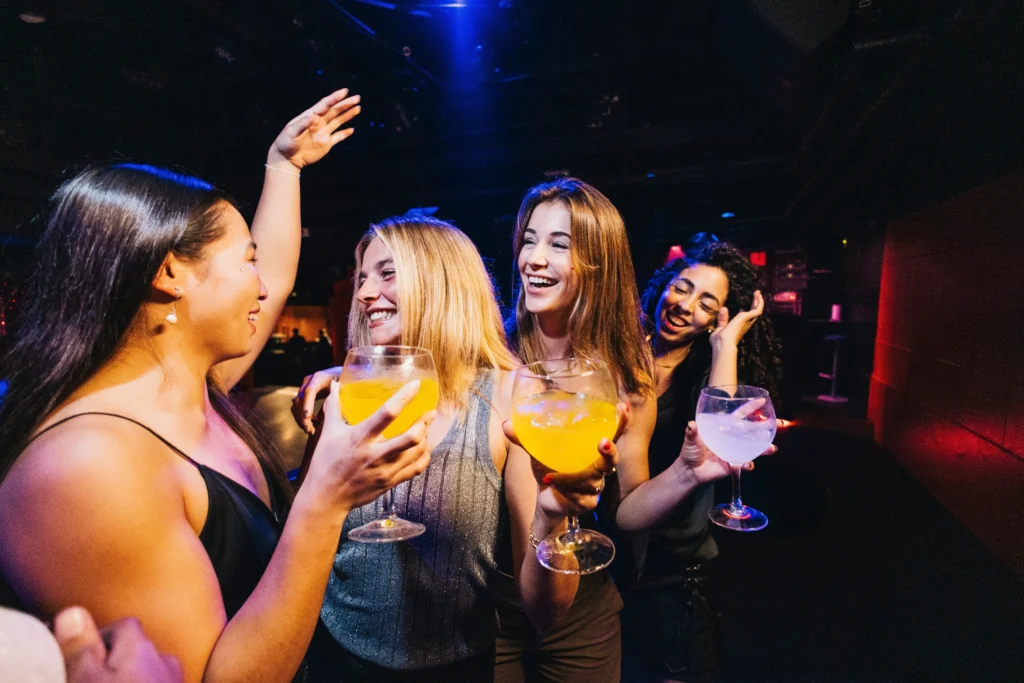 Skupina mladých žen v disco šatech a s koktejly v ruce se skvěle baví