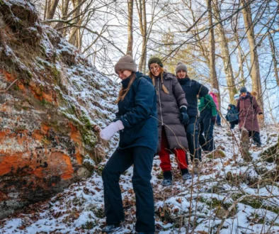 Skupina lidí jde na vycházku v horách. Mají teplé bundy. Jdou s kopce dolů