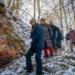 Skupina lidí jde na vycházku v horách. Mají teplé bundy. Jdou s kopce dolů