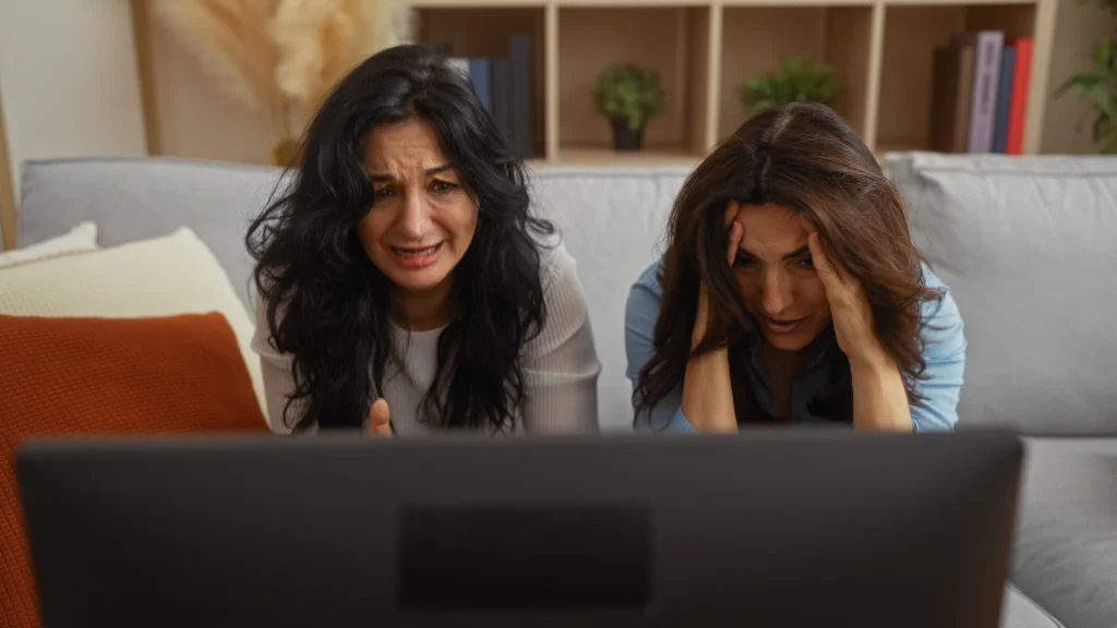 Dvě ženy se smutně dívají na televizní obrazovku, jedna pláče, druhá má hlavu v dlaních