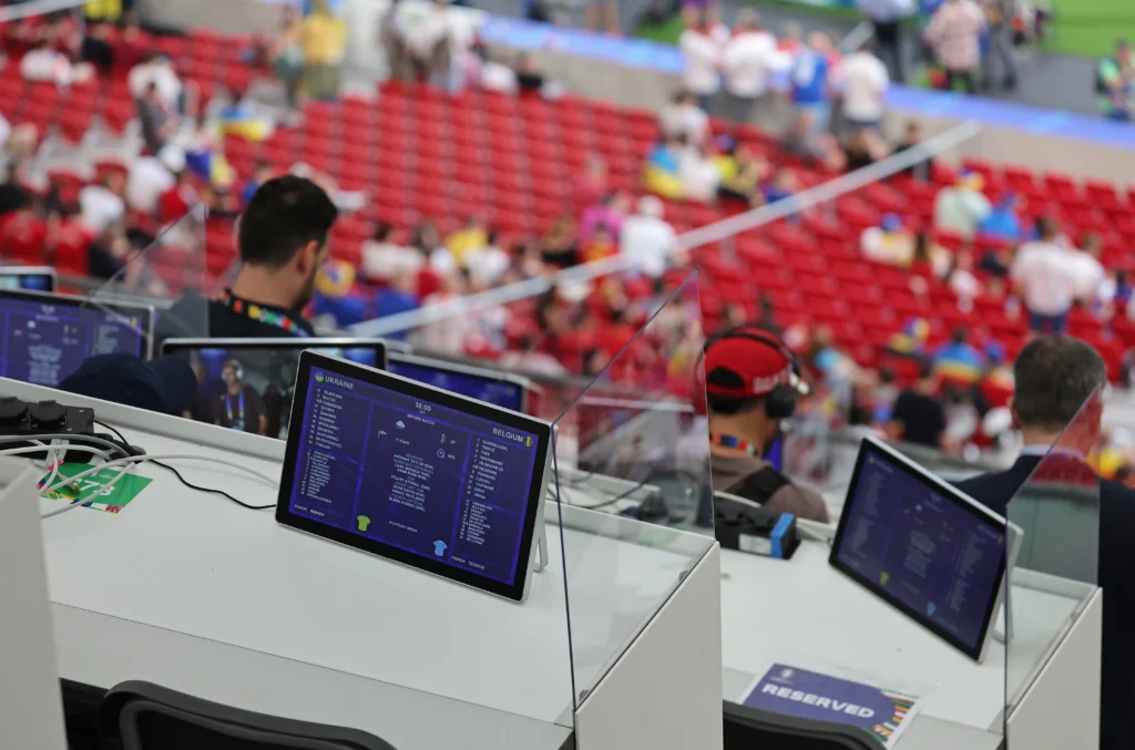 Stanoviště sportovních redaktorů na tribuně fotbalového stadionu, je vidět několik počítačů